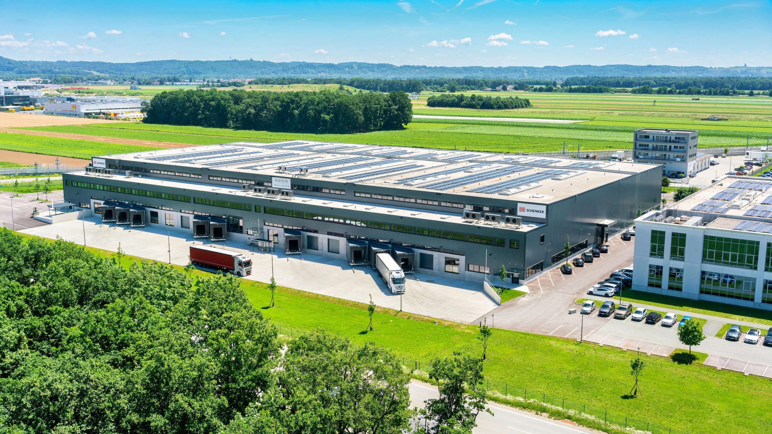 Logistikzentrum von Pletzer Immobilien mit Solarpanels auf dem Dach und anfahrenden LKWs.